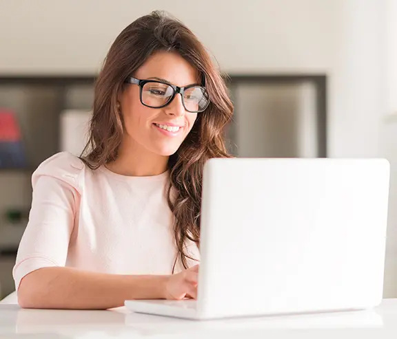 Una persona está sentada y sonriendo mientras trabaja en una computadora portátil.